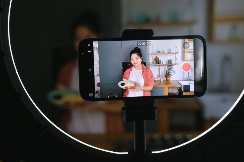 Девушка записывает кулинарное видео для соцсетей на смартфон, закреплённый в кольцевой лампе