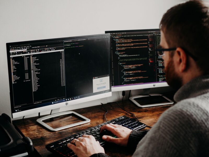 Разработчик программного обеспечения пишет код за столом с двумя мониторами