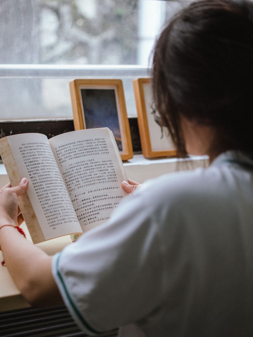 Девушка сидит у окна и читает книгу с китайским текстом