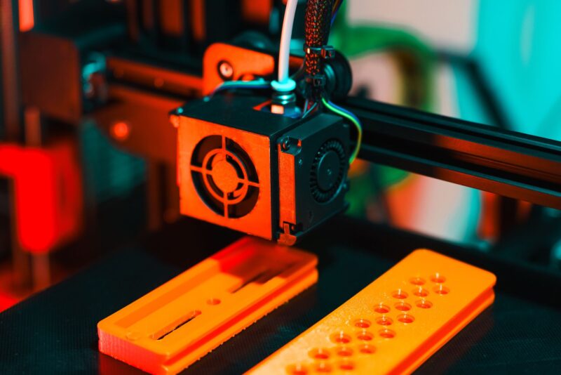 3D-принтер печатает оранжевые пластиковые детали прототипа