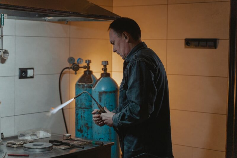 Мастер в синей рабочей рубашке работает ацетиленовой горелкой