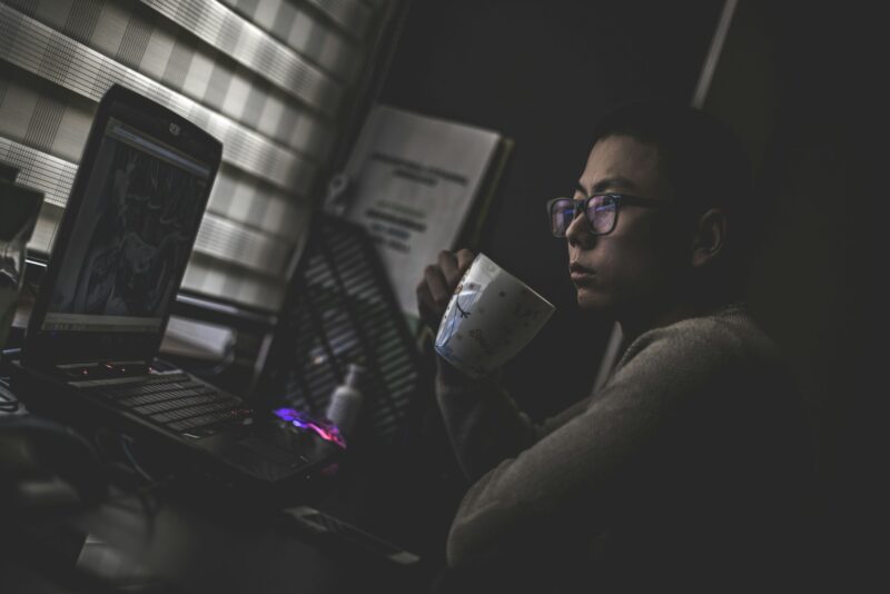 Разработчик с чашкой работает за ноутбуком дома вечером