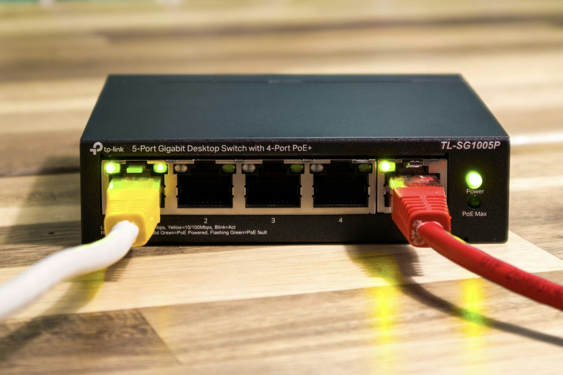 Небольшой сетевой коммутатор TP-Link с подключёнными Ethernet-кабелями на деревянном столе