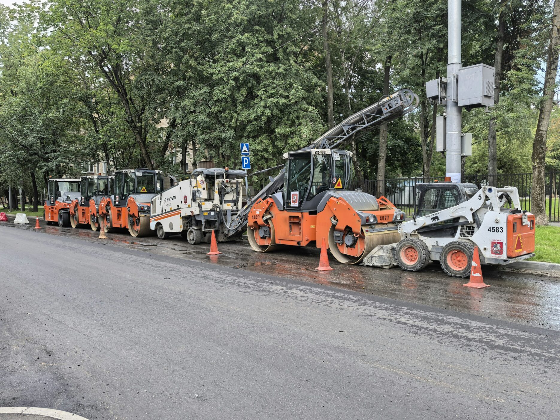 Дорожно-строительная техника выстроилась в ряд на мокром асфальте