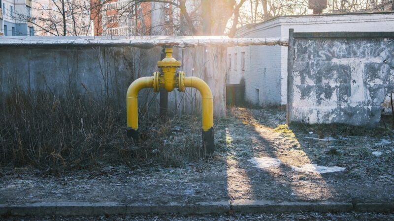 Жёлтая газовая труба с запорным краном на бетонной стене дома